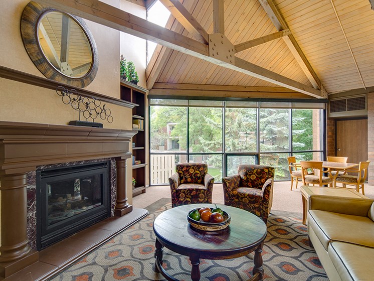 Community room with chairs facing fireplace, high ceilings with wooden archways, and large windows